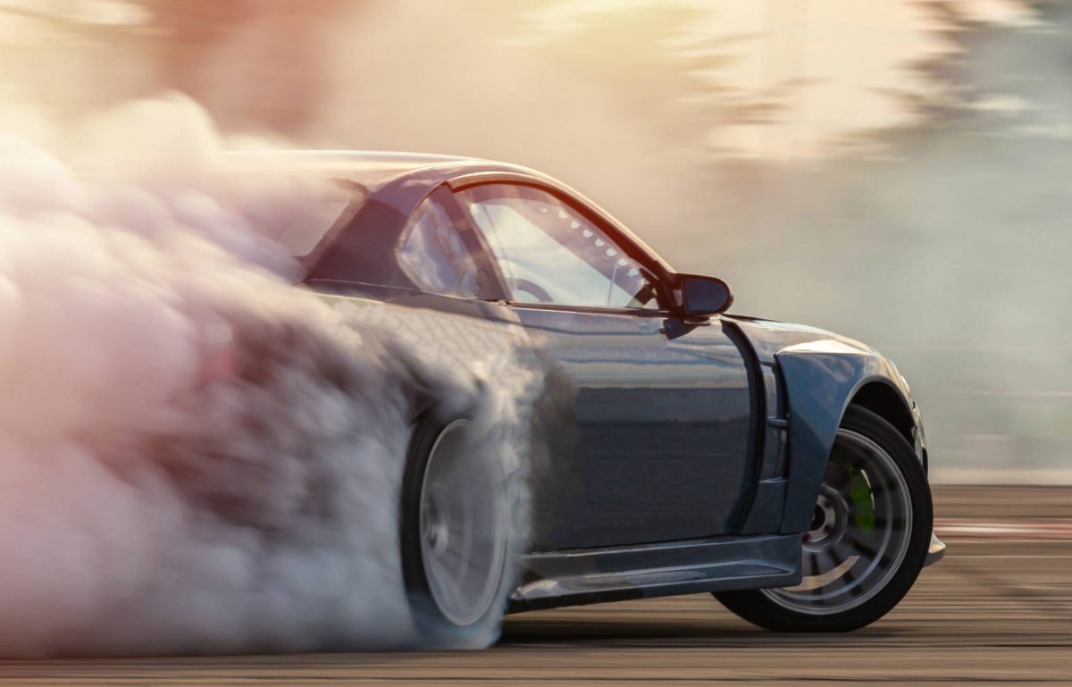A silver two-door sports coupe burning rubber on an outdoor course with smoke drifting up behind it.
