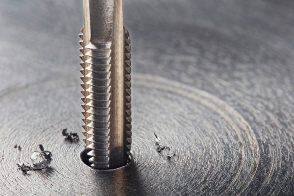 A threaded drill bit drilling into a piece of metal during thread milling. Burrs are sitting off to the side.