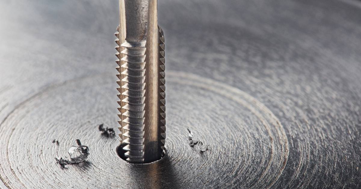 A threaded drill bit drilling into a piece of metal during thread milling. Burrs are sitting off to the side.