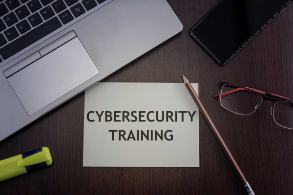 A birds' eye view of a desktop with a laptop, highlighter, pencil, glasses, and a note that says "Cybersecurity Training.