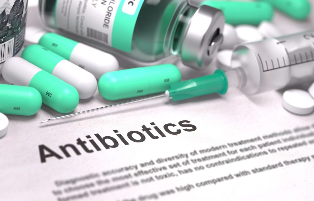 A sheet of paper with the word "Antibiotics" written on it, surrounded by capsule pills, tablets, and a needle.
