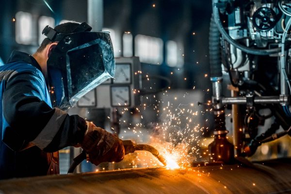 A man welding with protective gear on, including a welding helmet and gloves, while working in a factory.