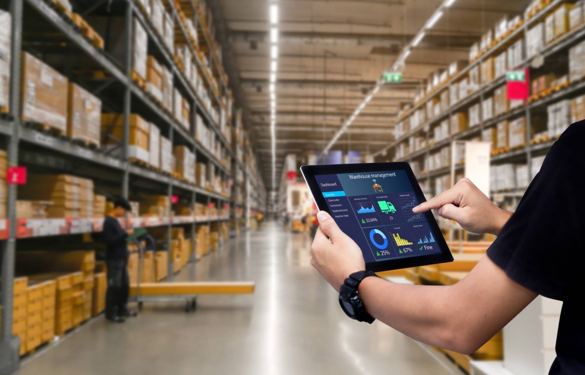A worker using a tablet to manage their inventory in a well-stocked smart warehouse. The worker scrolls through their data.