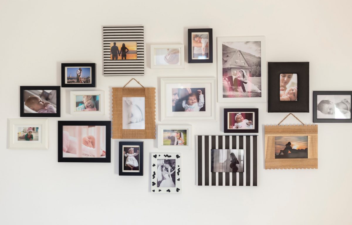 A photo gallery on a white wall with numerous photos of babies and couples surrounded by frames of different styles.