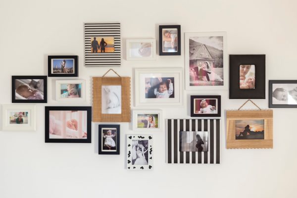 A photo gallery on a white wall with numerous photos of babies and couples surrounded by frames of different styles.