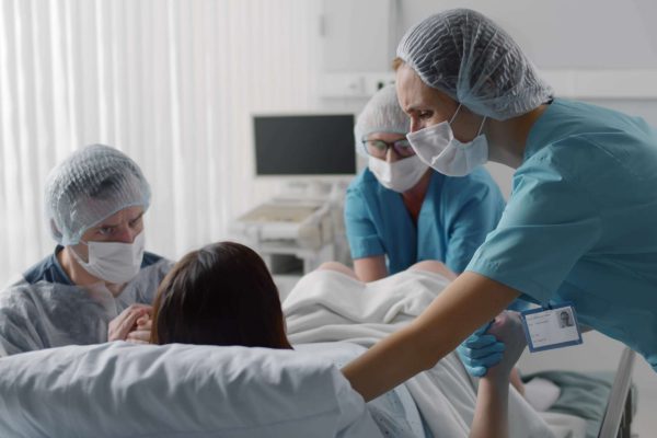 A woman is in a hospital bed giving birth. A doctor, a nurse, and her husband surround her for support.