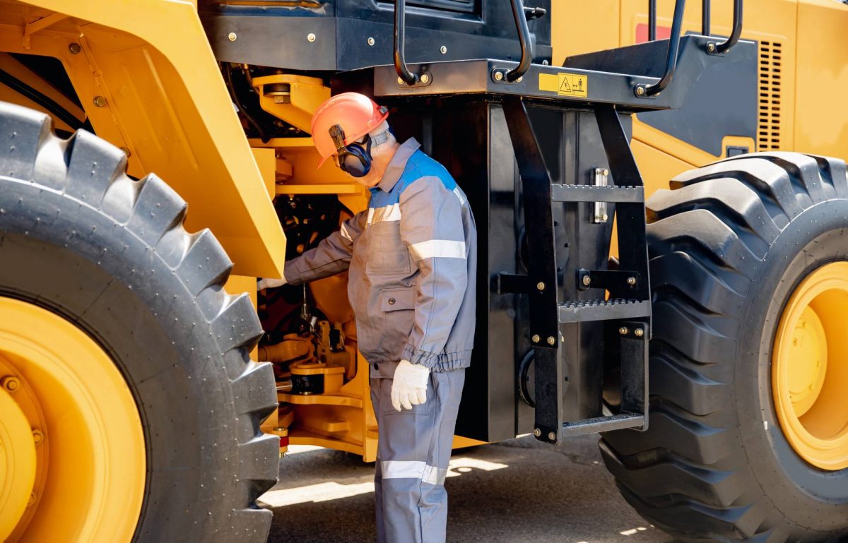 A mining worker takes a closer look at a piece of equipment he's working with. He wears a hard hat and protective earwear.