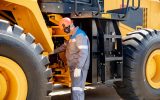 A mining worker takes a closer look at a piece of equipment he's working with. He wears a hard hat and protective earwear.