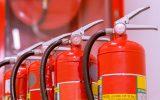 Four fire extinguishers lined up in a row in front of an "In Case of an Emergency, Break Glass" case.