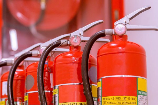 Four fire extinguishers lined up in a row in front of an "In Case of an Emergency, Break Glass" case.