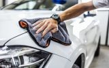 Someone wearing a watch and wiping their vehicle with a microfiber cloth. The car is white and freshly polished.