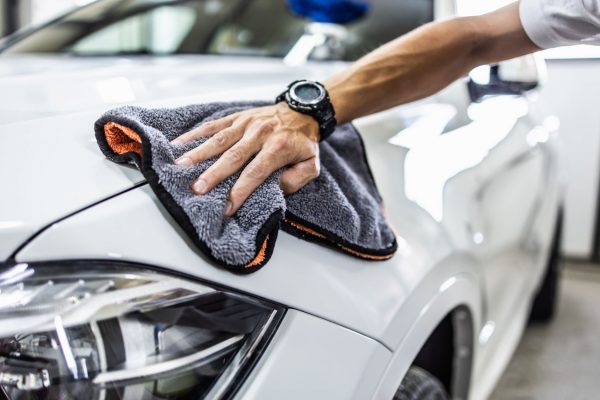 Someone wearing a watch and wiping their vehicle with a microfiber cloth. The car is white and freshly polished.