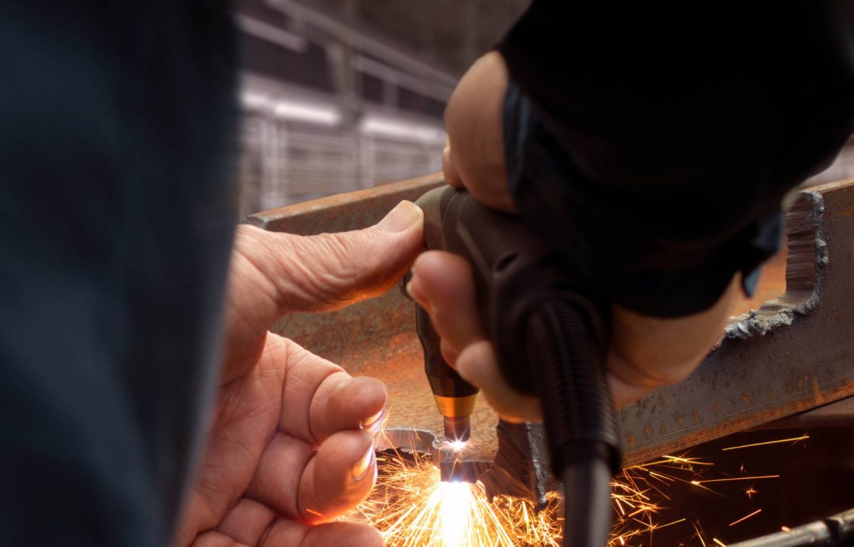 A person is cutting metal using a plasma cutting torch. The piece of metal appears rusty and old.