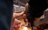 A person is cutting metal using a plasma cutting torch. The piece of metal appears rusty and old.