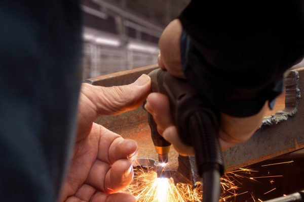 A person is cutting metal using a plasma cutting torch. The piece of metal appears rusty and old.