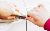 A person's hands holding two components of a Lishi lock pick to manipulate the lock of a car's door.