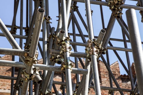 Scaffolding pipe clamp and parts on a construction site. There is a blue sky and a brick building in the background.