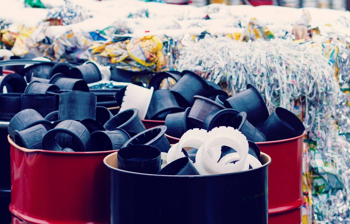 A large collection of paper, plastic, and other forms of waste is stacked, bound, and kept in red barrels.