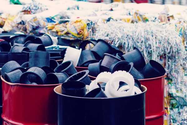 A large collection of paper, plastic, and other forms of waste is stacked, bound, and kept in red barrels.