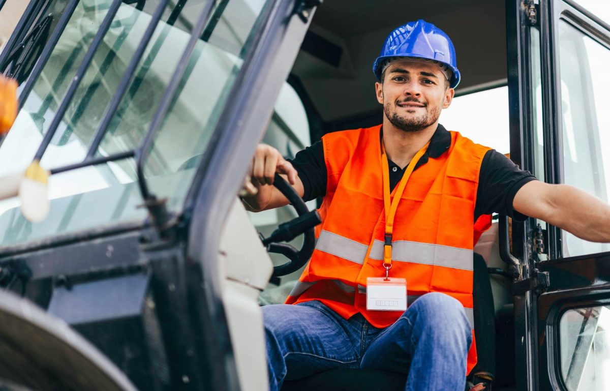 A skid steer operator stepping out of the vehicle. He is wearing a construction vest and hard hat to stay protected.