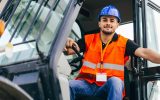 A skid steer operator stepping out of the vehicle. He is wearing a construction vest and hard hat to stay protected.