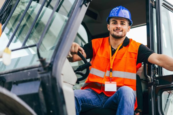 A skid steer operator stepping out of the vehicle. He is wearing a construction vest and hard hat to stay protected.