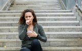 A woman sitting on an outdoor staircase and wearing athletic clothing. She is coughing into her hand.