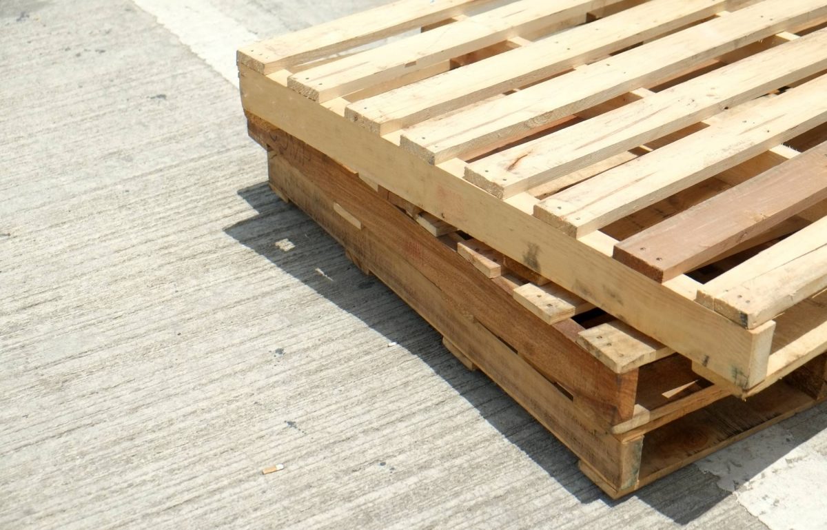 Three wooden pallets stacked on top of each other on a concrete surface. The sunshine hits the top wooden pallet.