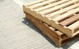 Three wooden pallets stacked on top of each other on a concrete surface. The sunshine hits the top wooden pallet.