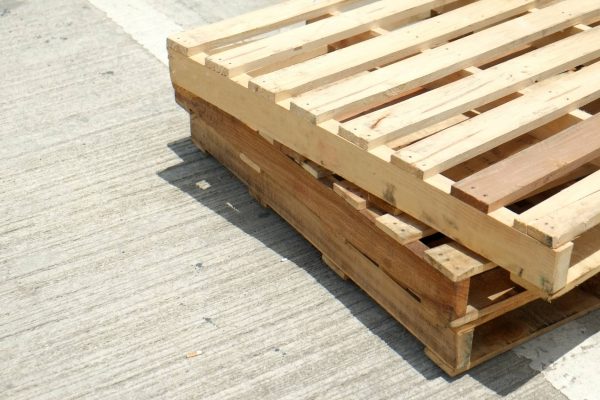 Three wooden pallets stacked on top of each other on a concrete surface. The sunshine hits the top wooden pallet.