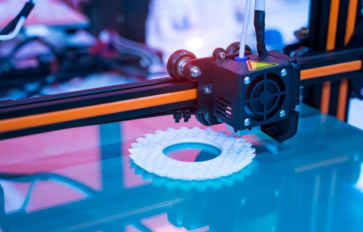 A large 3D printing machine with a small moving square is printing a white, round piece on top of a plastic base.