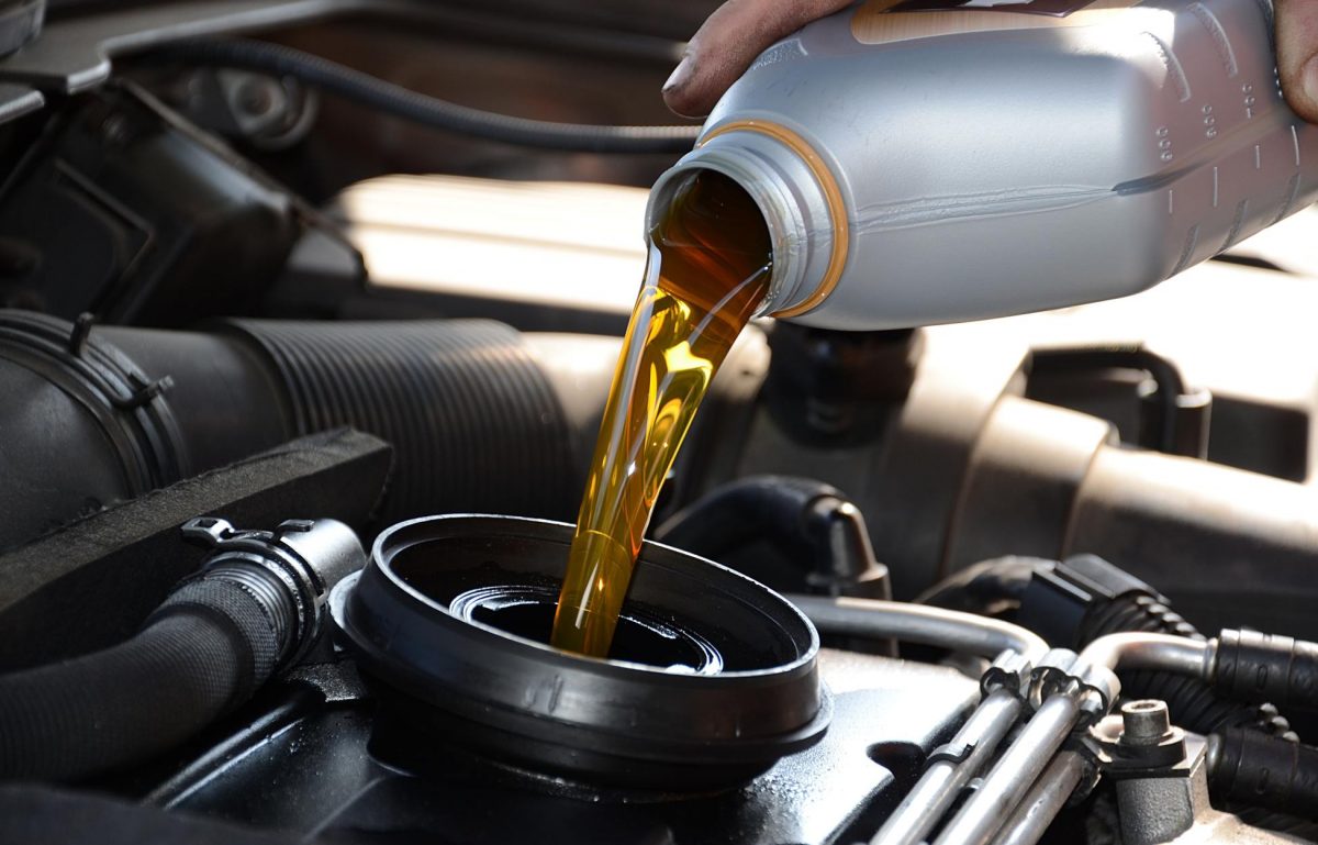 A person is pouring oil into an engine. The oil is yellow in color and is coming out of a gray container.