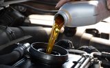 A person is pouring oil into an engine. The oil is yellow in color and is coming out of a gray container.