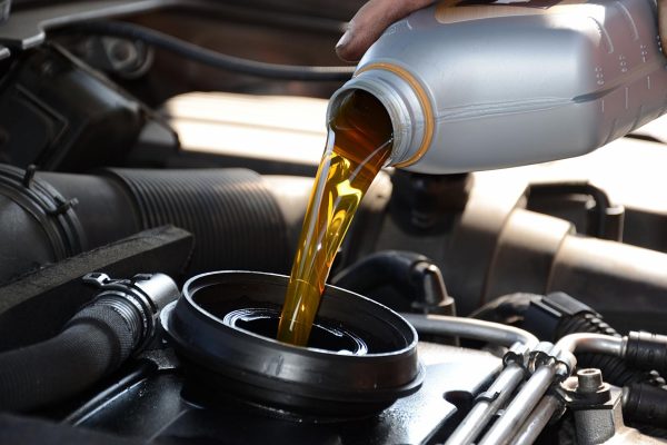 A person is pouring oil into an engine. The oil is yellow in color and is coming out of a gray container.