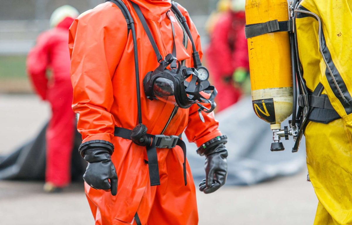 Several people outside wearing full chemical protection gear, complete with a suit, mask, and gloves.