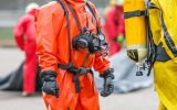 Several people outside wearing full chemical protection gear, complete with a suit, mask, and gloves.