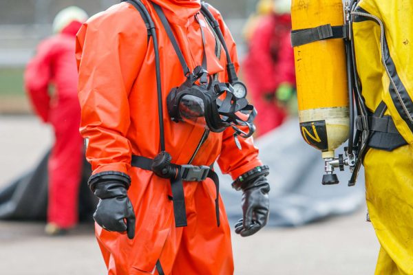 Several people outside wearing full chemical protection gear, complete with a suit, mask, and gloves.