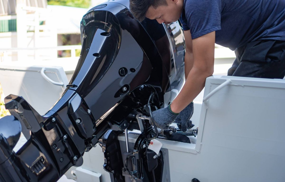 A man wearing a blue shirt, blue gloves, and blue pants is working on a black boat engine on a white boat.