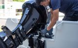 A man wearing a blue shirt, blue gloves, and blue pants is working on a black boat engine on a white boat.