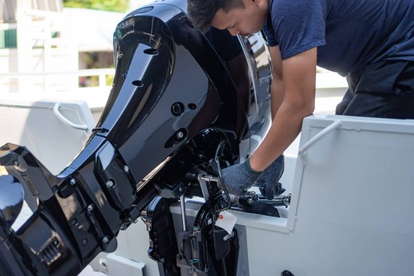 A man wearing a blue shirt, blue gloves, and blue pants is working on a black boat engine on a white boat.