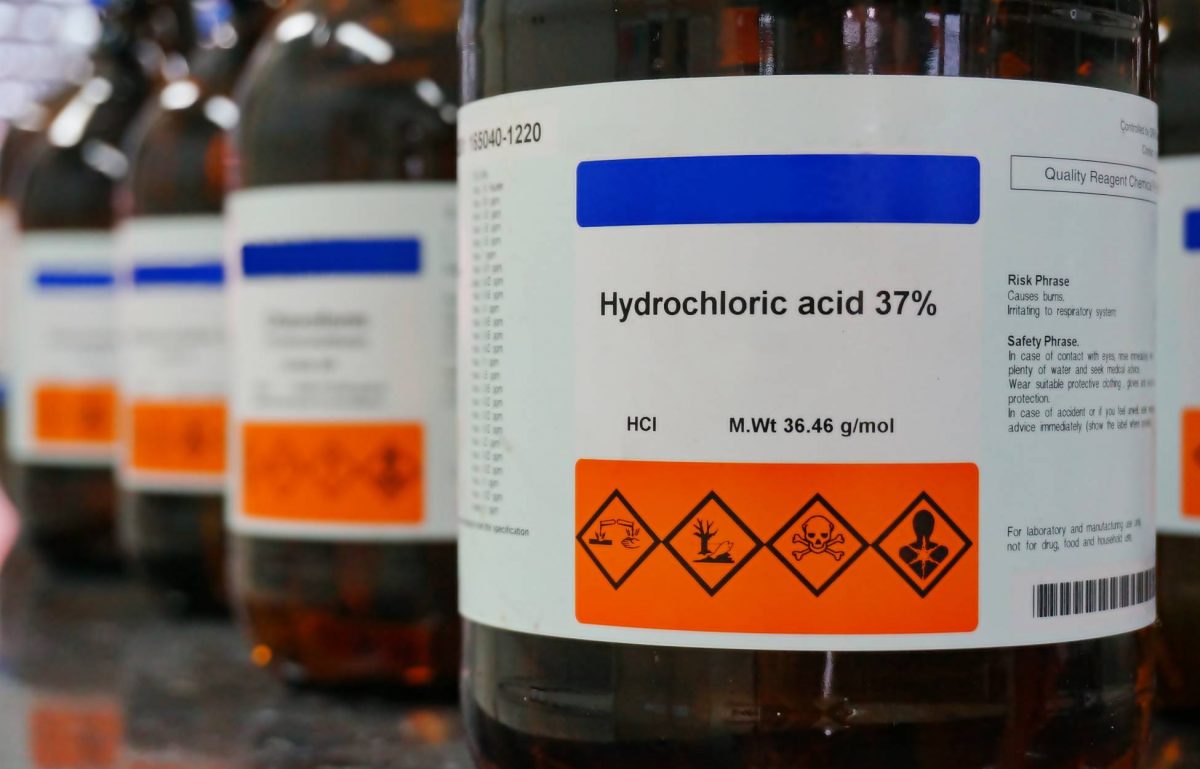 A close-up of a row of bottles with white labels on them. The front label says "Hydrochloric acid 37%" and has a hazard warning.