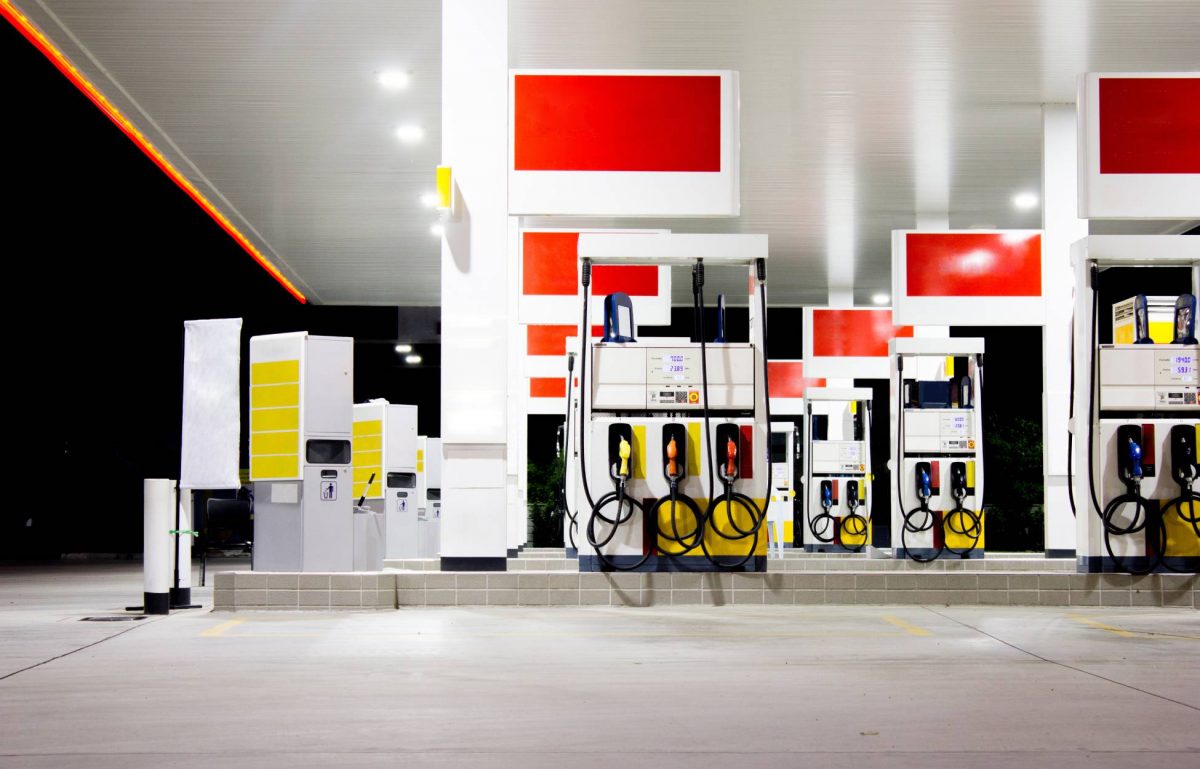 Red and yellow gas pumps of a local gas station at night. The pumps are illuminated by lights on the ceiling.