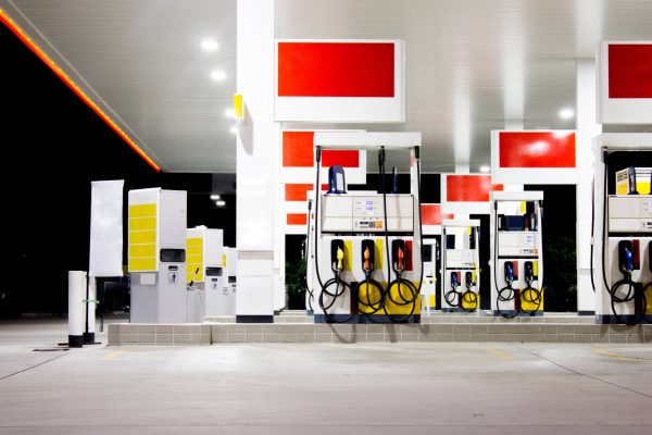 Red and yellow gas pumps of a local gas station at night. The pumps are illuminated by lights on the ceiling.