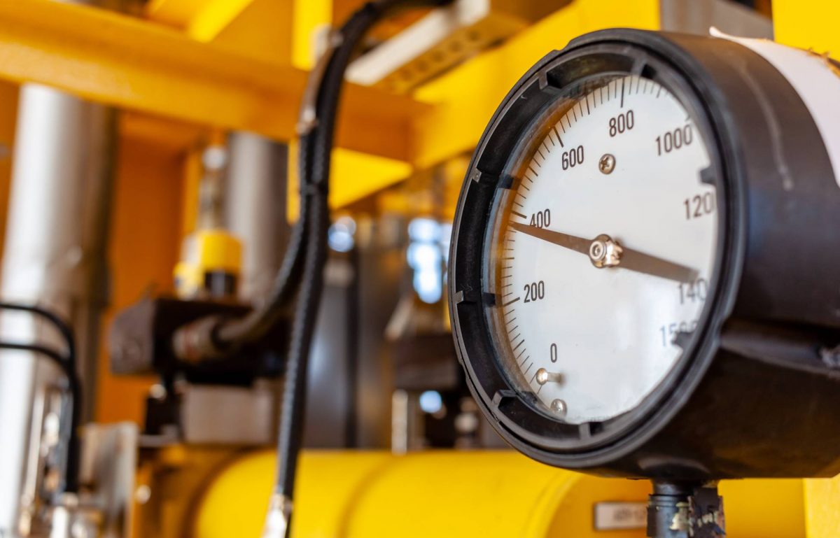 A close-up of an industrial pressure gauge displaying a reading of nearly 400 psi. The surrounding pipes are yellow.