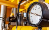 A close-up of an industrial pressure gauge displaying a reading of nearly 400 psi. The surrounding pipes are yellow.