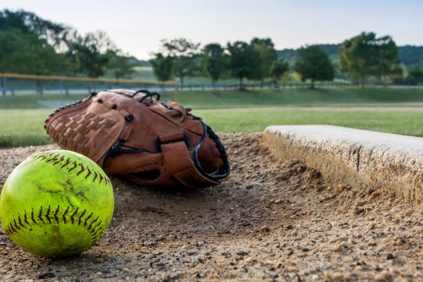 A softball and a glove sitting on the diamond. The pitcher's mound is next to the ball and glove and looks used.