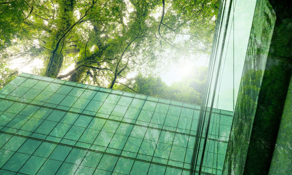 An eco-friendly glass office building with trees outside. The trees outside reflect off the glass on the building.