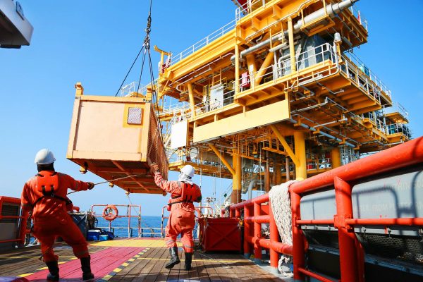 A two-man offshore rigging crew on the rig as they watch a moving box overhead. The box is moving via crane.