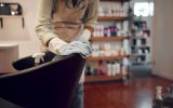 A woman cleaning the back of a styling chair in her salon. She's wearing gloves and using a cloth to wipe it down.