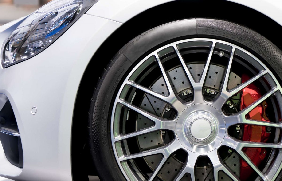 A close-up of the front right wheel well on a white sports car. The wheel features alloy rims and red brake calipers.